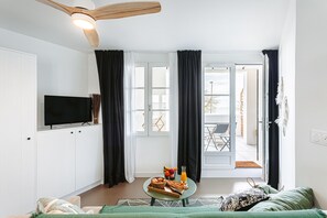 Ett modernt vardagsrum med en platt-TV, ett matbord med frukosttillbehör, en soffa och en takfläkt.