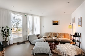 Un salon moderne comprenant un canapé, un fauteuil et un pouf, une petite table d’appoint et une lampe.