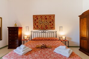 Un lit bien fait, recouvert d’une couvre-lit à motifs, deux lampes de chevet, une table de chevet en bois, une armoire en bois et une œuvre d’art encadrée accrochée au mur.
