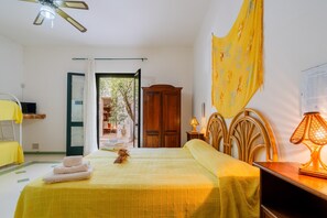 A room with a bed, a wooden wardrobe, a table with a lamp, and a ceiling fan.
