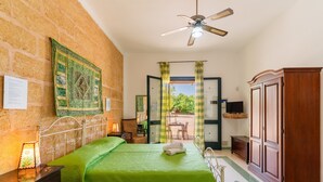 Une chambre avec une couvre-lit verte, un ventilateur de plafond, une armoire en bois et une vue sur l’extérieur, visible à travers une porte.