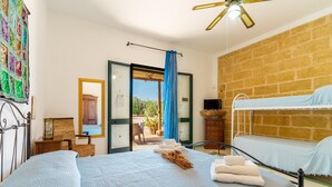 Un dormitorio con cama, literas, ventilador de techo, ventana con vistas y puerta que da a un área exterior.