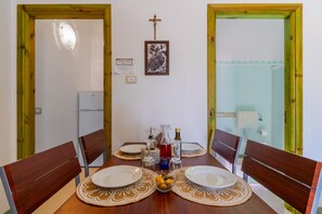 Une table à manger dressée avec des assiettes, des verres et un saladier de fruits, entourée de chaises en bois.