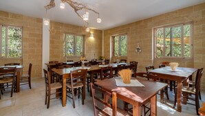 Un comedor amplio con varias mesas y sillas de madera, ventanas grandes y una lámpara de techo original.