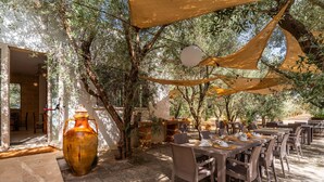 Un área de comedor al aire libre con mesas y sillas, un jarrón grande y un muro de piedra.