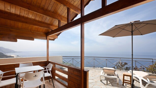 Una terraza de madera con una mesa y sillas, suelo de piedra y vista al mar.