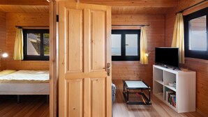 Interior de una cabaña de madera con una cama, un televisor y una estantería.