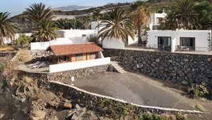 Una propiedad costera con un muro de contención de piedra, un pequeño edificio con techo de tejas y palmeras.