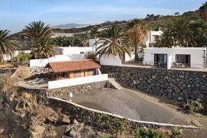 Una propiedad costera con un muro de contención de piedra, un pequeño edificio con techo de tejas y palmeras.