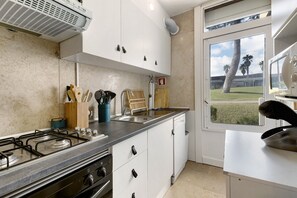 A kitchen with a gas stove, white cabinets, a dishwasher, and a window with a view of palm trees.