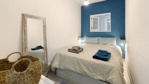 Une chambre à coucher comprenant un lit, un miroir, une lampe fixée au mur et un panier en osier.