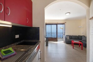 Eine moderne Küche mit roten Schränken, ein Essbereich mit einem roten Tisch und ein Balkon mit Blick.