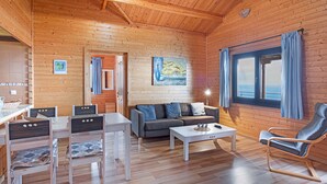 A wooden cabin interior with a dining area, sofa, and a rocking chair. - Holiday Home 'Moijama 12' with Sea View, Shared Pool and Wi-Fi (Los Llanos de Aridane)