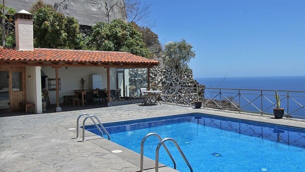 A swimming pool with metal ladders, a patio area with tables and chairs, and a view of the sea. - Holiday Home 'Moijama 12' with Sea View, Shared Pool and Wi-Fi (Los Llanos de Aridane)