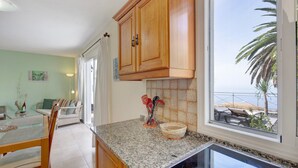 A kitchen with wooden cabinets, a granite countertop, and a view of the beach through a window. - Holiday Home 'Moijama 6' with Sea View, Shared Pool and Wi-Fi (Los Llanos de Aridane)