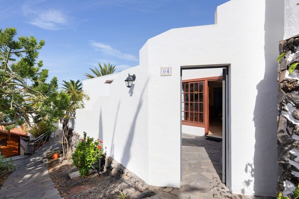 A white building with a stone wall, a wooden door, and a potted plant.