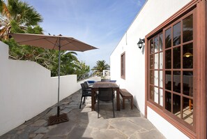 A patio with a table and chairs, a large umbrella, and a stone floor.