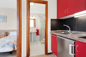 Une chambre d’hôtel compacte, dotée d’une kitchenette, d’une salle de bain avec douche et d’un lit recouvert d’une courtepointe aux couleurs vives.