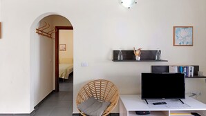 A living room with a TV, a wicker chair, a bookshelf, and a doorway leading to another room. - Apartment 'Moijama 1' with Shared Pool, Private Terrace and Wi-Fi (Los Llanos de Aridane)