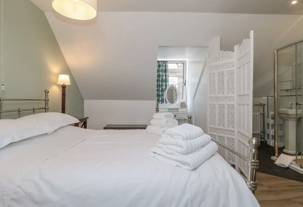 A hotel room with a neatly made bed, a bedside table with a lamp, a bathroom with a mirror, and a decorative white partition.