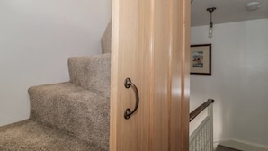 Una puerta de madera con un pomo curvo, una escalera alfombrada y un cuadro enmarcado en la pared.