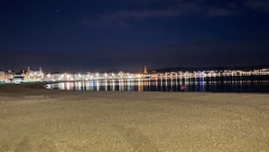 Escena nocturna de playa con un paisaje urbano al fondo.