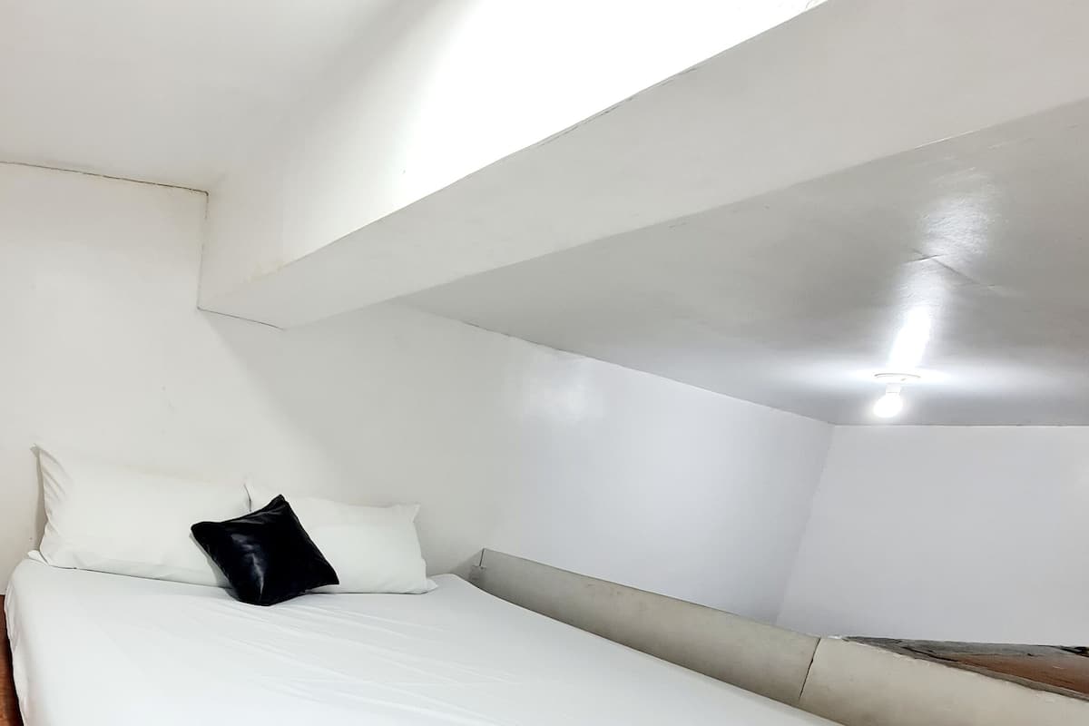 A small, minimalist bedroom with a single bed, white walls, and a sloped ceiling.