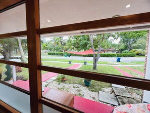 A view through a window with a wooden frame, a red bench, and a grassy area with trees and a red canopy.