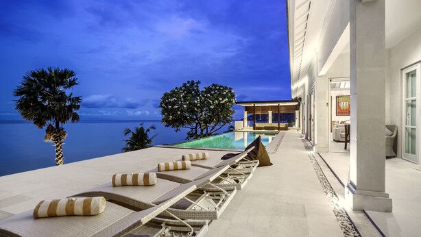 A poolside area with lounge chairs and a view of the ocean at dusk. - Villa Eden Roc by Alfred in Bali (Karangasem)