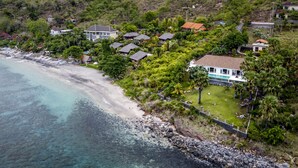An aerial view of a coastal residential area with houses, a beach, and a clear view of the ocean. - Villa Eden Roc by Alfred in Bali (Karangasem)