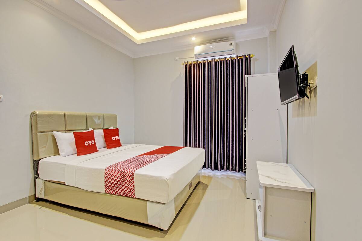 Quarto de hotel bem arrumado com uma cama, uma TV de tela plana na parede e um aparelho de ar condicionado acima da cama.