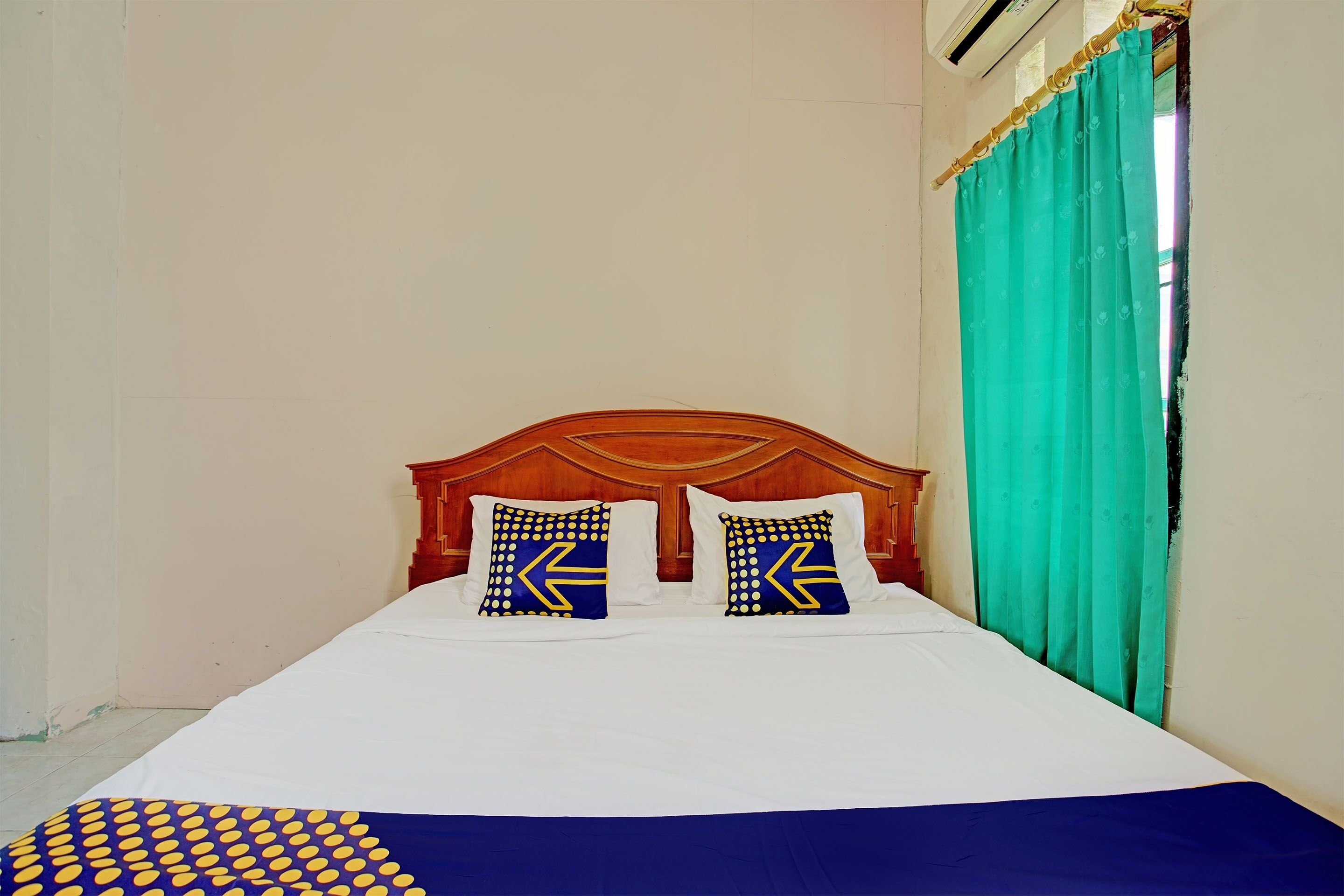 A bed with a wooden headboard, two pillows with geometric patterns, a white bedspread, and a teal curtain.