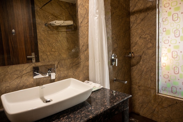 Un baño con pared de mármol, lavamanos blanco, cabina de ducha de vidrio y un perchero para toallas.