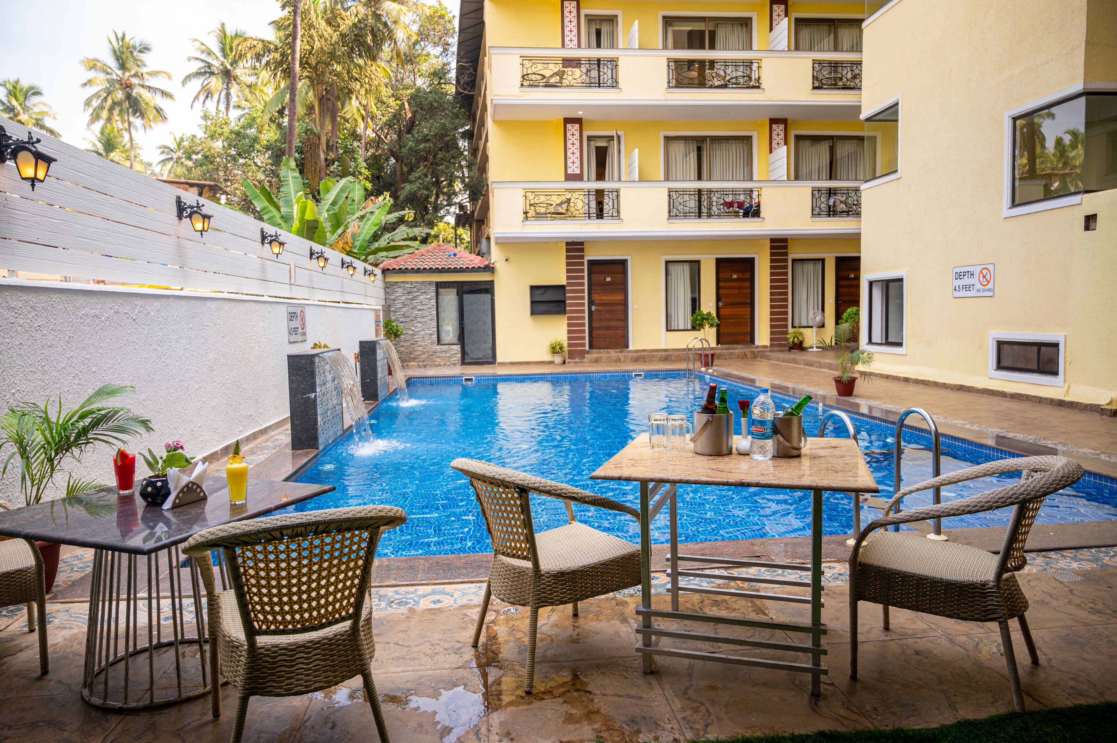 A swimming pool with a table and chairs, surrounded by a building with balconies and a sign indicating a depth limit.