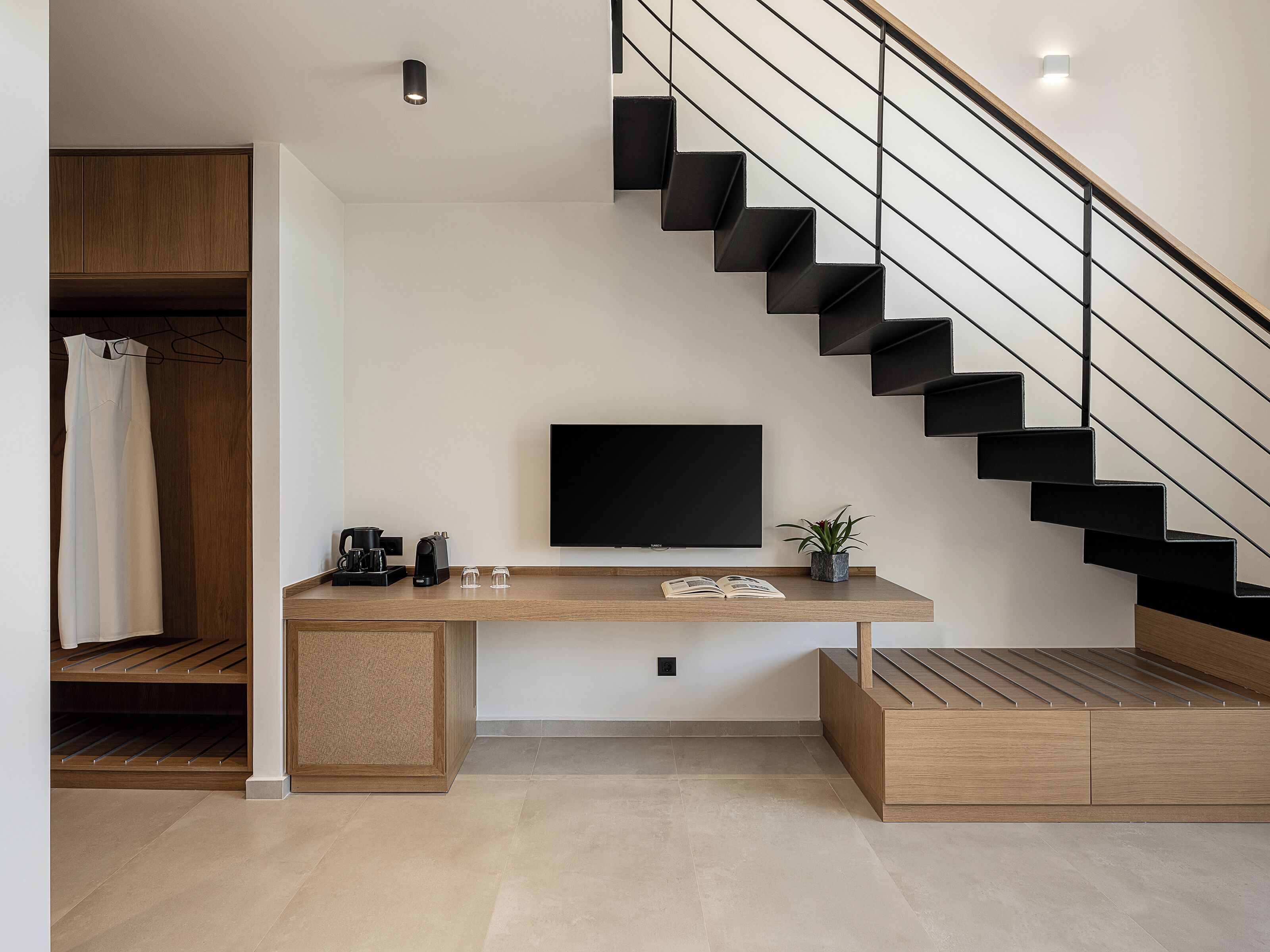 Un espacio habitable moderno con un escritorio de madera, un televisor de pantalla plana, una escalera y un armario.