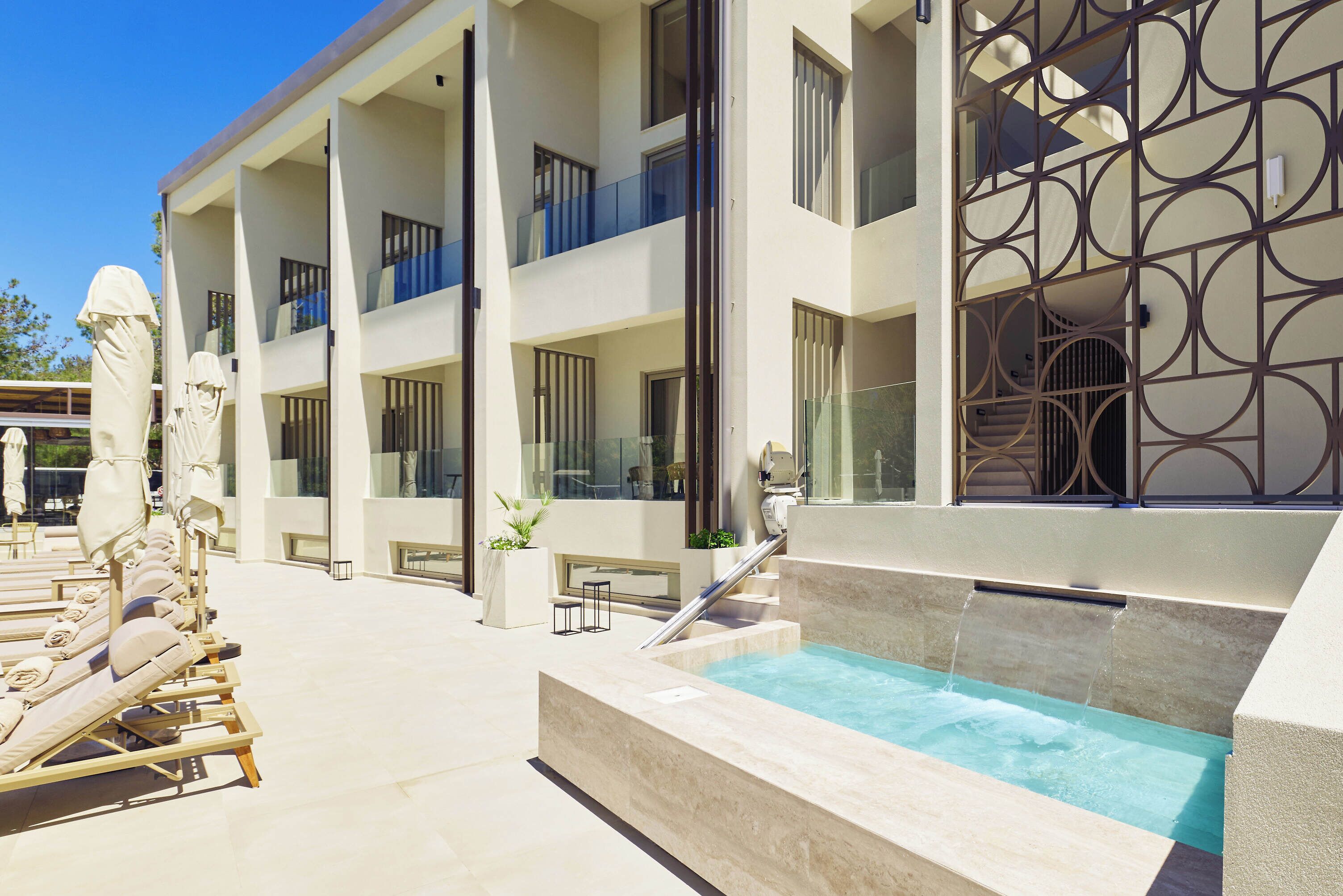 A modern hotel with a pool area, sun loungers, and a geometric decorative wall.