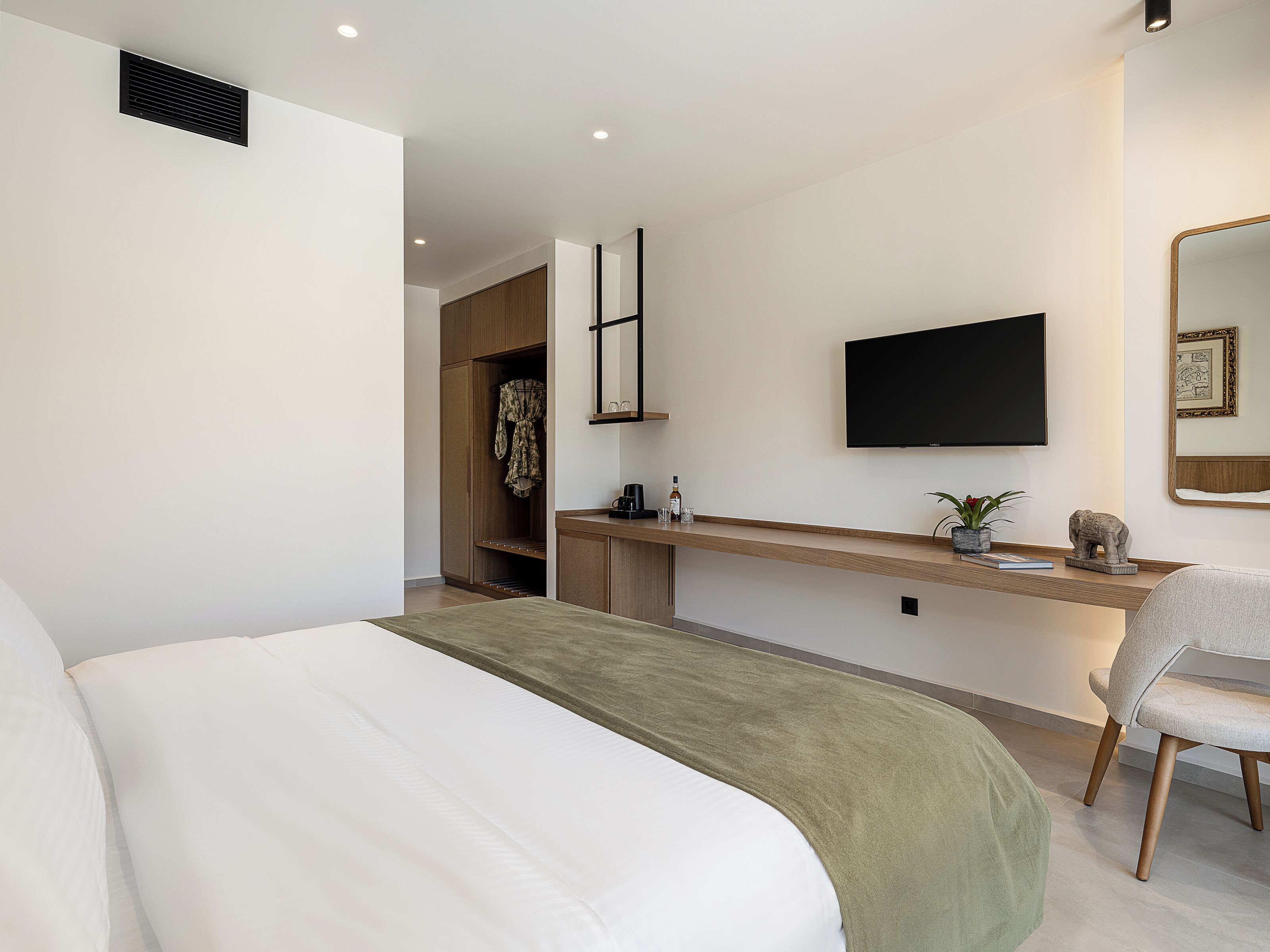 Habitación de hotel moderna con una cama grande, un escritorio con televisor de pantalla plana, un espejo y una pequeña estatua.