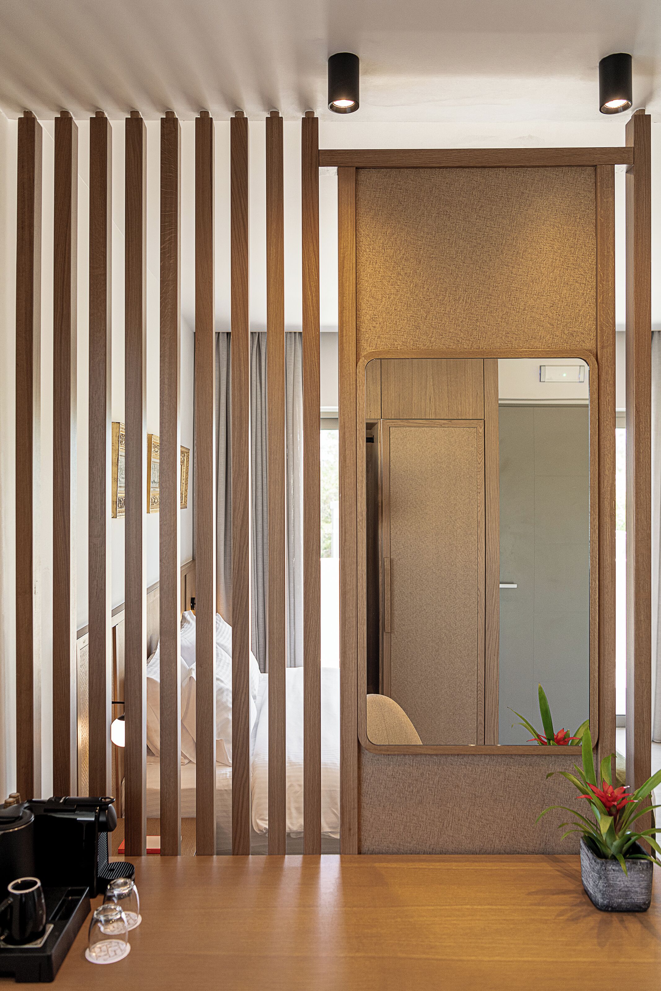 A hotel room with a wooden partition, a small table with a coffee maker and glasses, and a potted plant.
