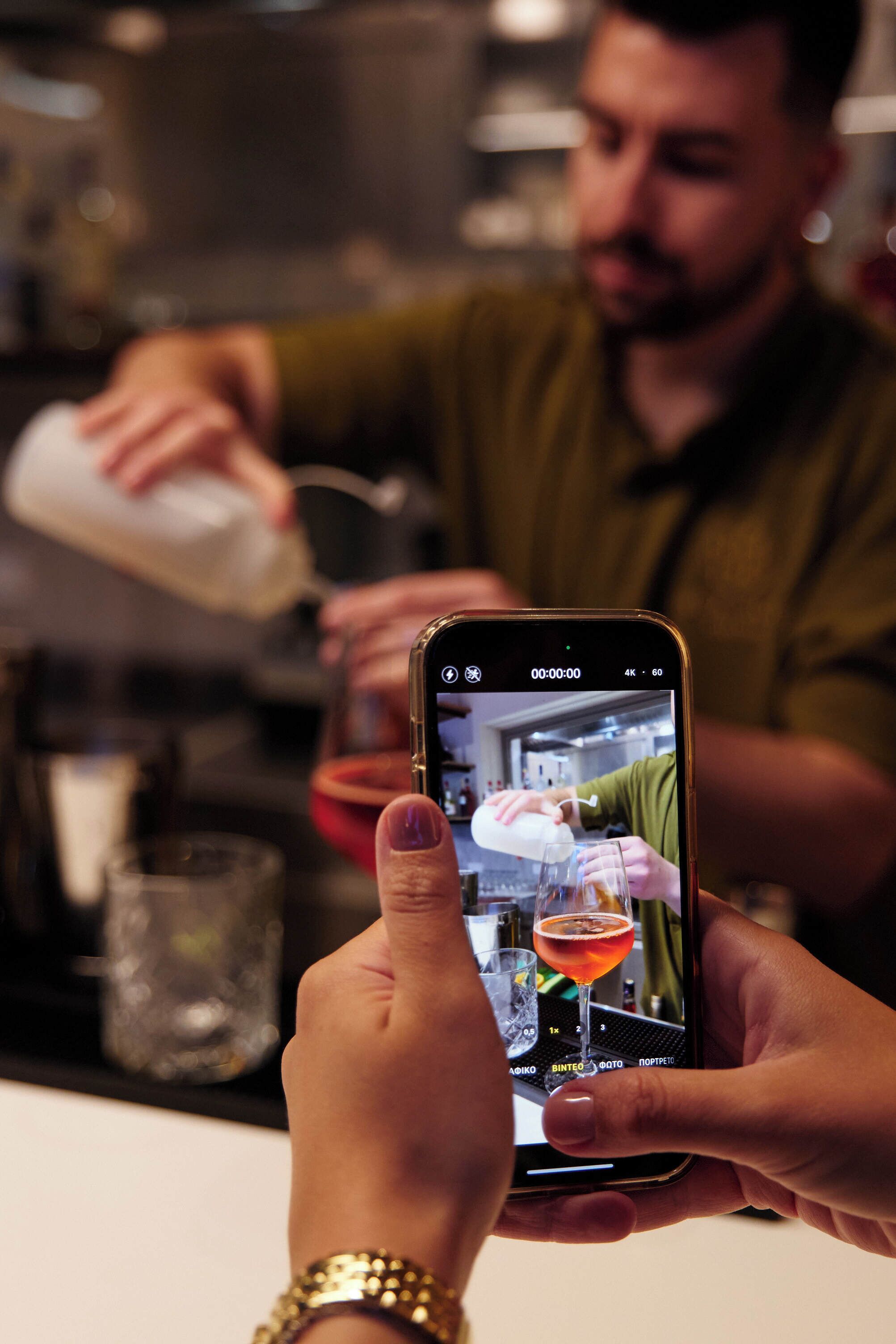 A person holding a smartphone with a video of a bartender preparing a drink.