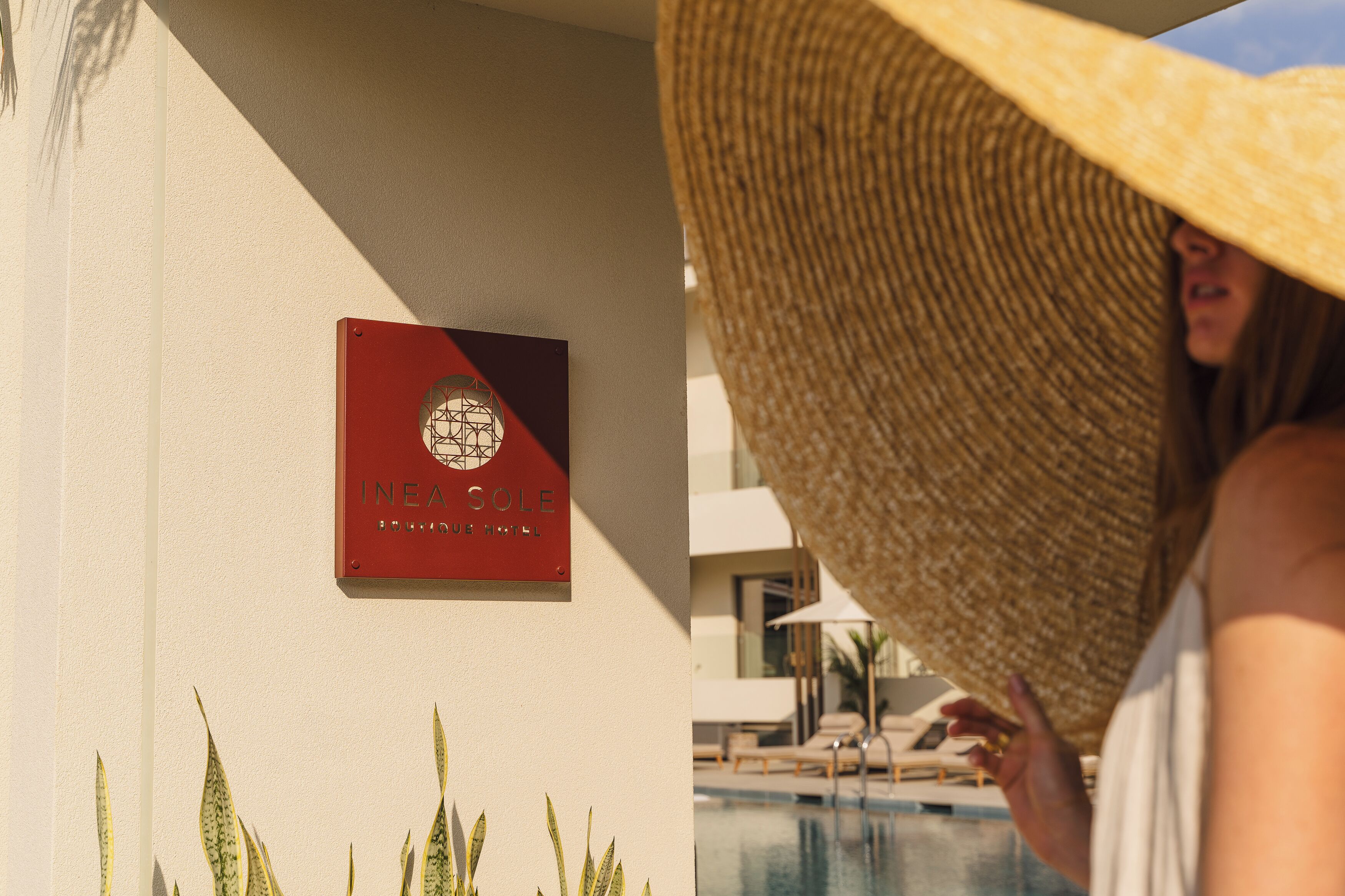 Placa do hotel INEAL SOLE, área de piscina com espreguiçadeiras e uma pessoa de chapéu de palha.