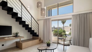 A modern living room with a black staircase, a flat-screen TV, a wooden console table, and a seating area with a sofa and two round tables. - Inea Sole Boutique Hotel (Chania)