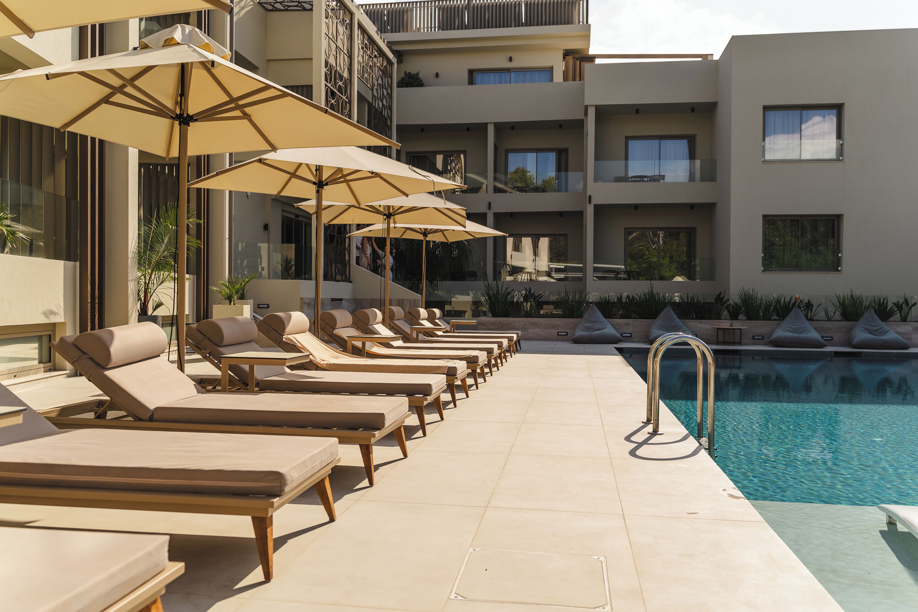 A poolside area with sun loungers and umbrellas, a pool, and a building with balconies.