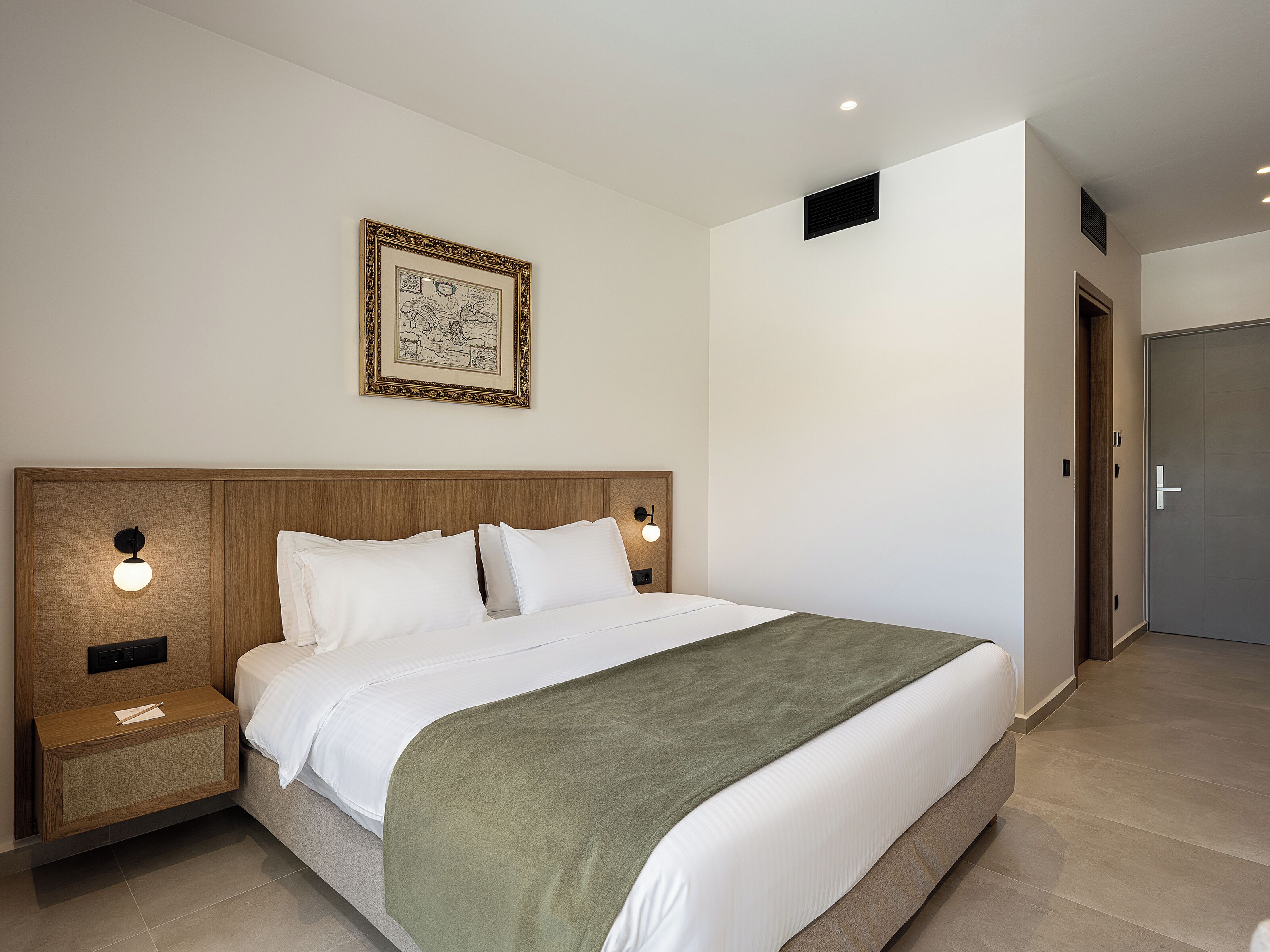 Ein modernes Hotelzimmer mit einem großen Bett, einem Nachttisch, einem Wandbild und einer Tür.