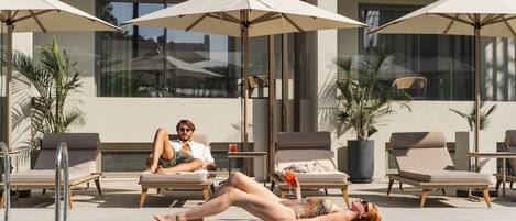 A poolside area with lounge chairs and umbrellas, a pool, and a building with large windows.