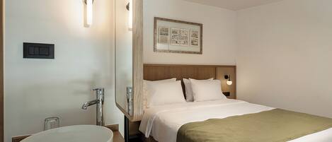 A hotel room with a large round sink, a bed with a green throw, and a framed picture on the wall.
