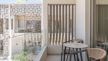 A balcony with a glass partition, a round table with chairs, and a view of the building's interior.
