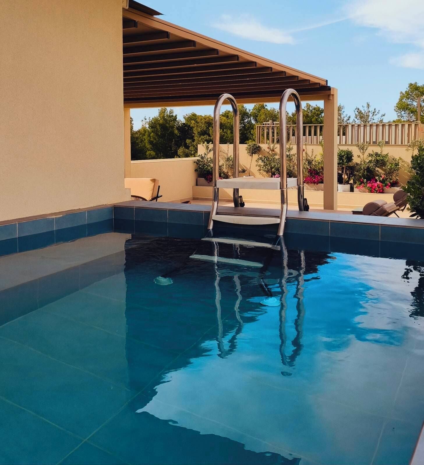 Una piscina con una escalera de metal, un pérgola y mobiliario de exterior.