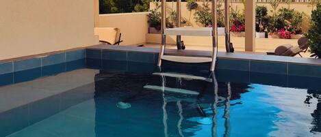 Una piscina con una escalera de metal, un pérgola y mobiliario de exterior.
