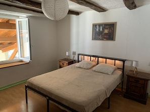 Un dormitorio con cama, mesitas de noche, lámpara colgante, un cuadro en la pared y ventana con vista a una estructura de madera.