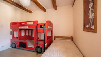 Una habitación con una cama individual, una cama en forma de autobús rojo de dos pisos, vigas de madera, una pared blanca y un personaje de dibujos animados enmarcado.